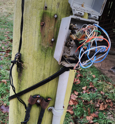 telephone pole with phone box spewing wires, and several obviously cut cables attaches