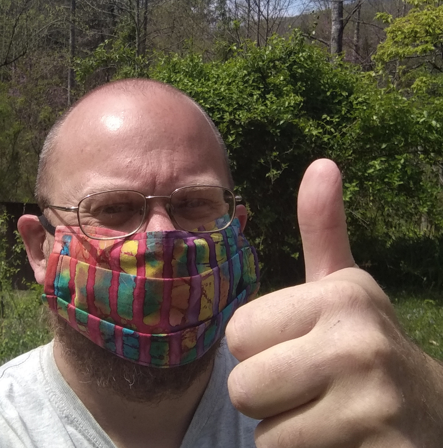 Joey in a rainbow tie-die mask,
holding a thumb up.